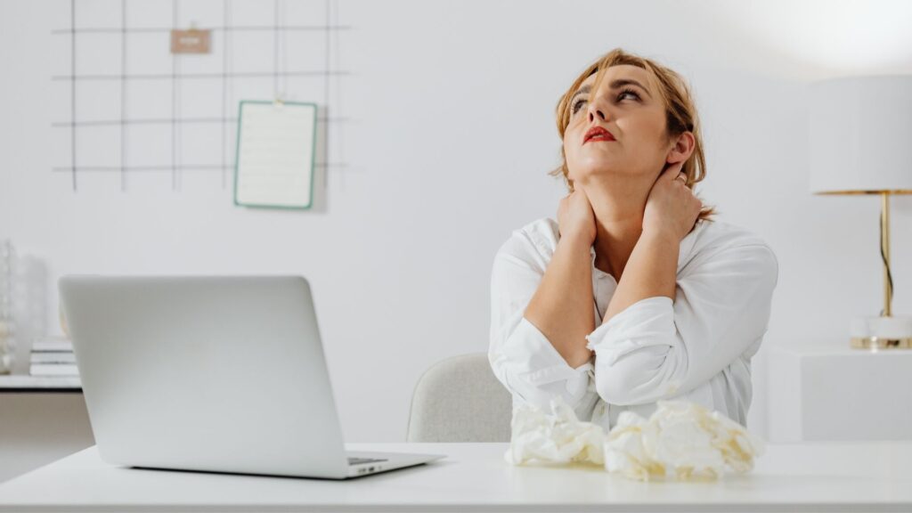woman sitting at a computer holding her neck in pain