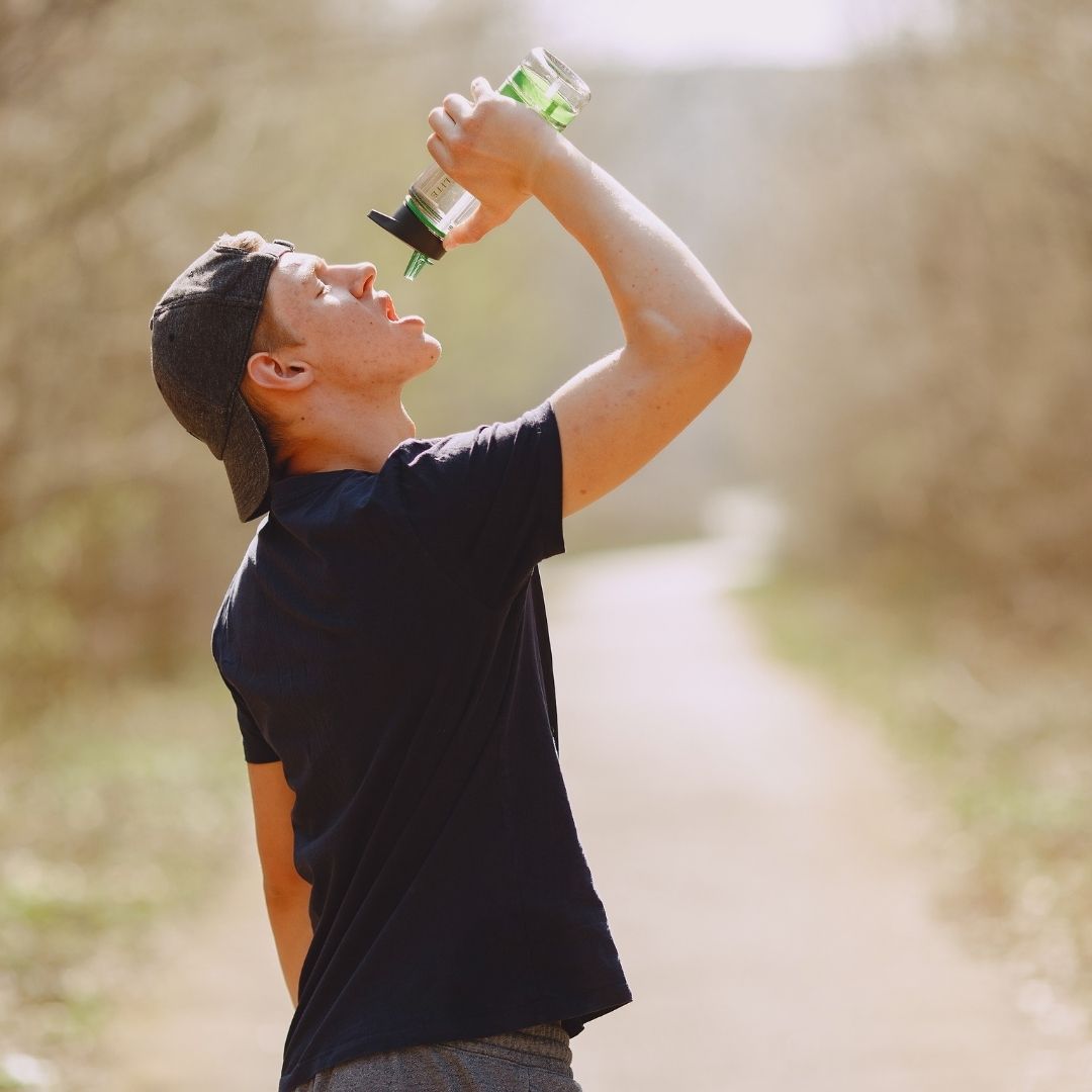 A man outdoors on a walk, drinking water.